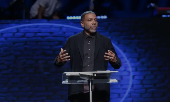 Creflo Dollar preaching against a blue-backlit brick wall